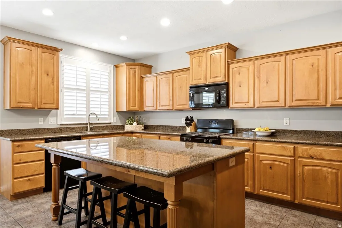 Spacious kitchen featuring light wood cabinetry, granite countertops, a central island with bar seating, and tile flooring