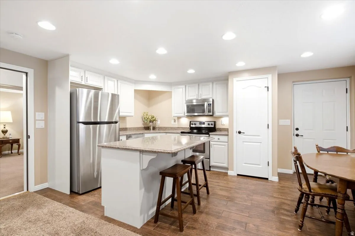 Kitchen featuring a center island with countertop seating, stainless steel appliances, white cabinetry, and wood-finish flooring