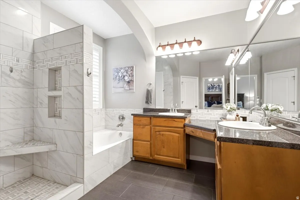 Full bathroom featuring a walk-in shower with built-in niches and seating, a separate soaking tub, and a dual vanity with wood cabinetry and dark countertops