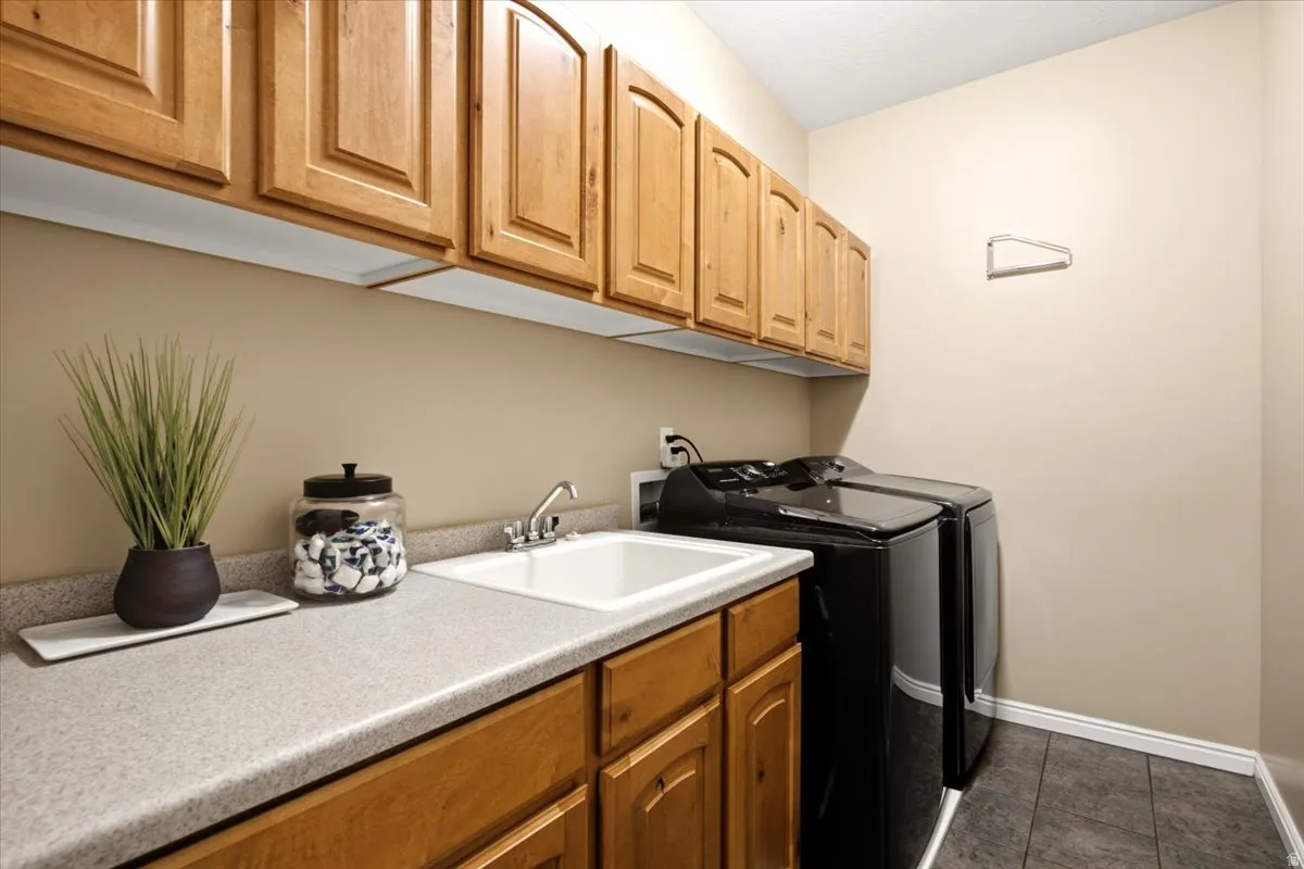 Laundry area featuring wood cabinetry, a utility sink, light-toned countertops, and dark tile flooring
