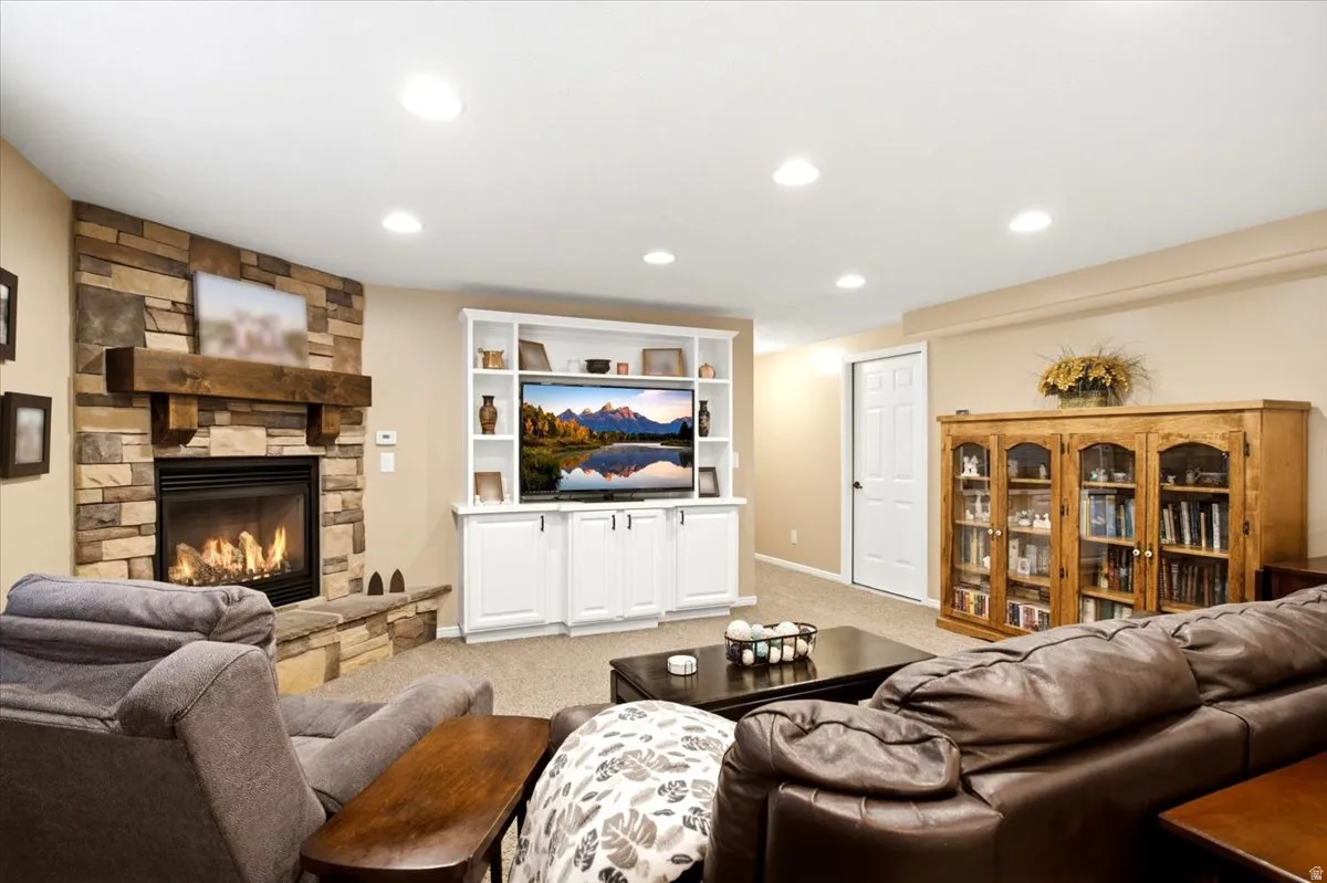 Stacked stone fireplace with a substantial wood mantel, built-in media center with shelving, recessed lighting, neutral carpeting, and a white paneled door