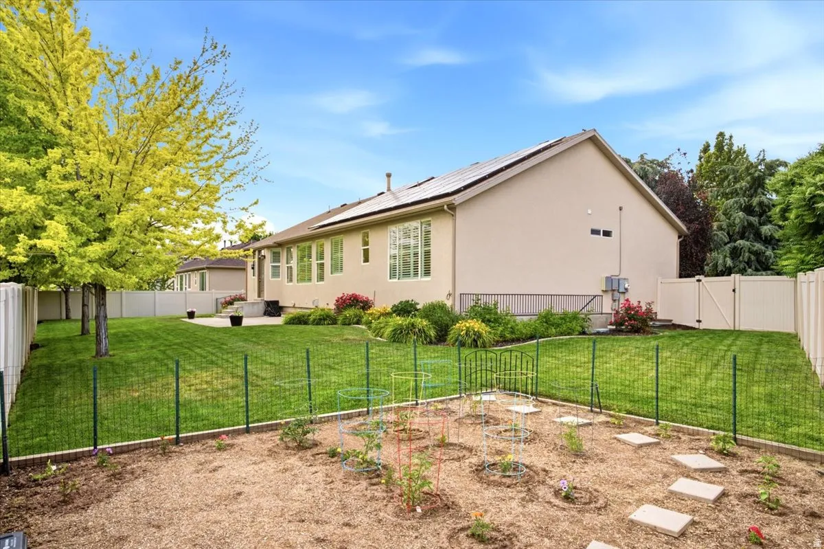 Expansive backyard featuring a dedicated garden area with stepping stones, a green wire fence, and mature trees