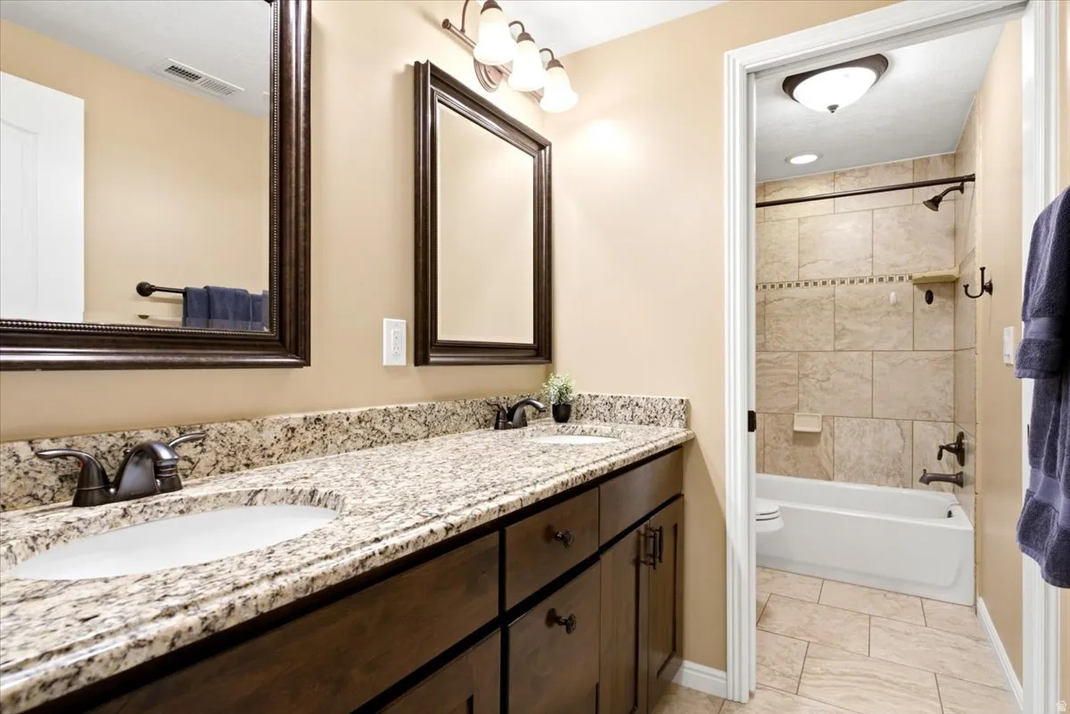 Bathroom vanity featuring dual under-mount sinks set into a light-toned countertop, framed mirrors, and dark wood-finish cabinetry