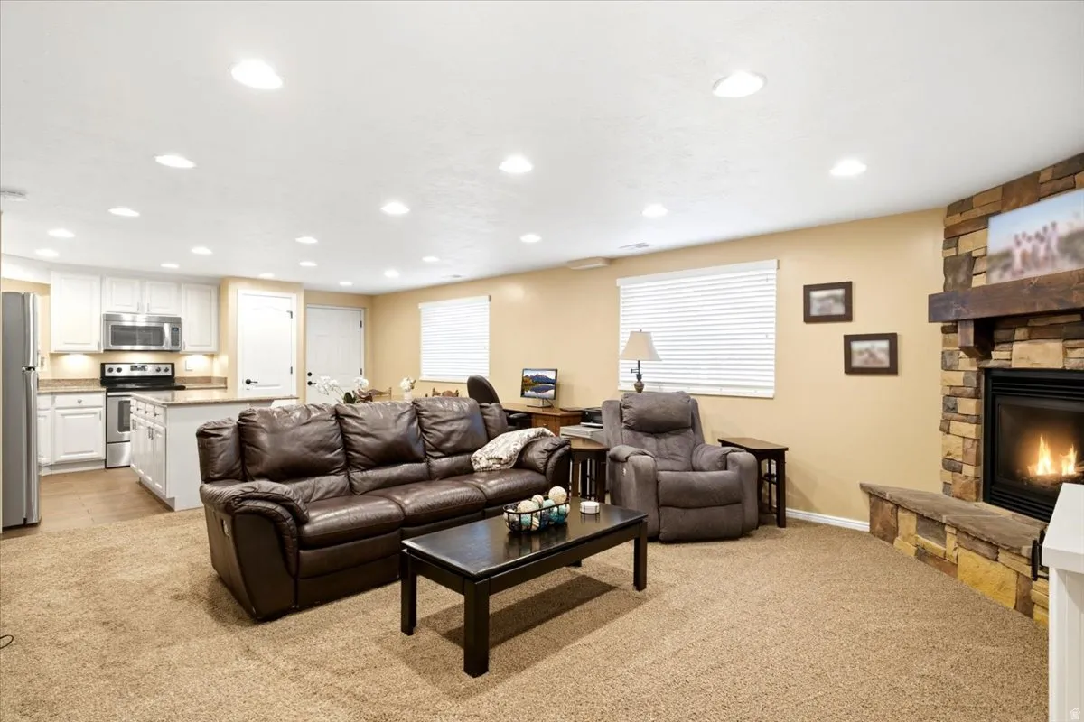Open-concept living space featuring a stone-faced fireplace with a wood mantel, recessed lighting, and a kitchen area with white cabinetry, stainless steel appliances, and a central island