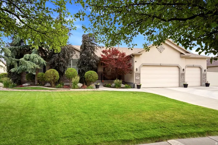 Exterior featuring a stucco facade, stone accents, two-car garage, mature landscaping, and a manicured lawn