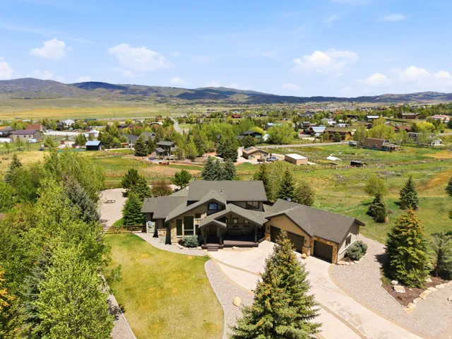 Stone and wood-sided residence featuring a multi-car garage, expansive driveway, mature landscaping, and a surrounding natural landscape