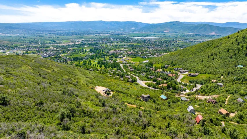 Expansive mountain landscape featuring a valley community, surrounded by rolling green hillsides