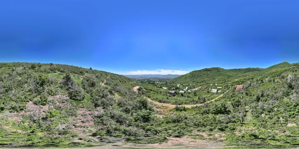 Expansive mountain landscape featuring lush green foliage and distant structures