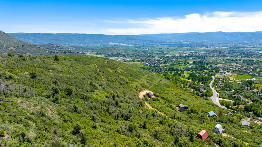 Expansive hillside property featuring diverse terrain, established greenery, and distant residential areas