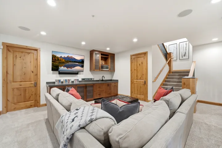 Entertainment area featuring a built-in wet bar with wood cabinetry and dark stone countertop, recessed lighting, and light-toned carpeting