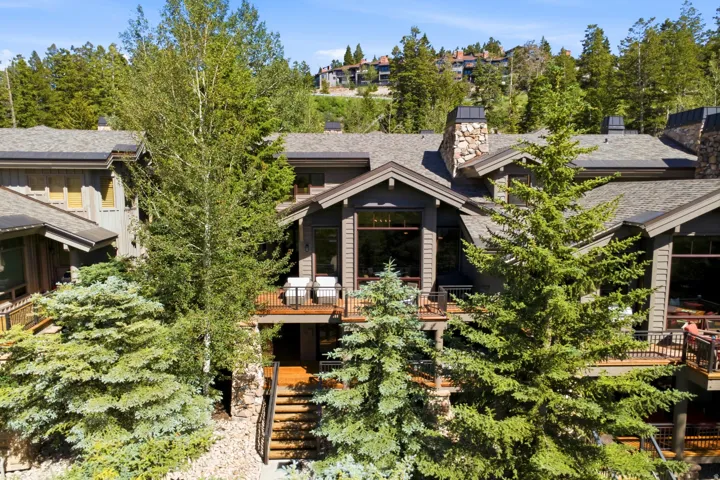 Multi-level property featuring dark wood siding, multiple decks with dark railings, and a stone chimney