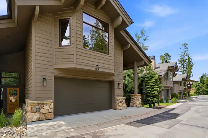Exterior showcasing natural wood siding, a prominent two-car garage, and stone accent pillars