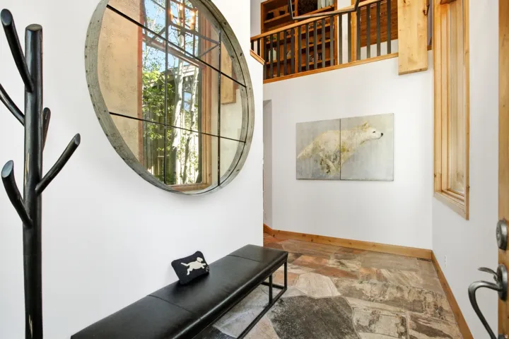 Foyer with multi-toned stone flooring, white walls, and a round window with dark grid details