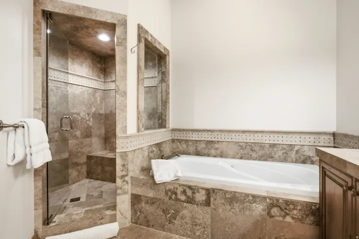 Tiled bathroom featuring a glass-enclosed shower with an integrated bench, a built-in soaking tub, and a vanity with an integrated countertop