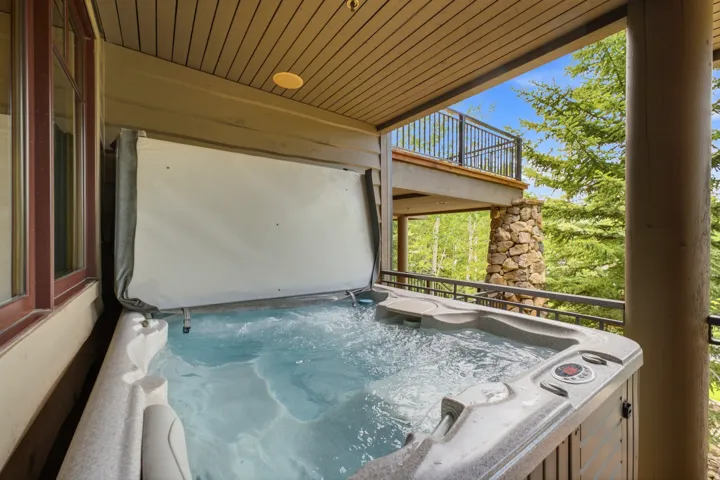 Outdoor hot tub with an open cover under a covered balcony