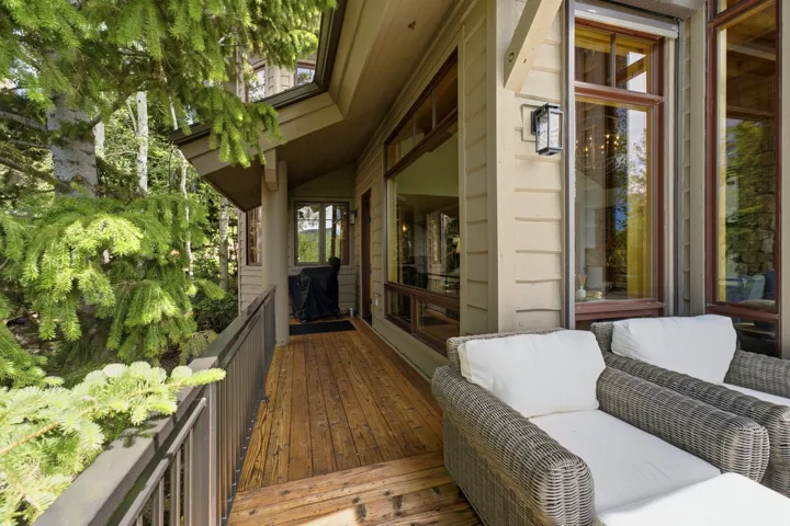 Wood-finish deck with a dark metal railing, featuring horizontal siding, large windows, and an outdoor wall sconce