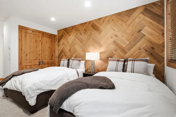 Bedroom featuring a herringbone wood-finish accent wall, twin beds with upholstered bases, recessed ceiling lighting, and natural wood bi-fold doors
