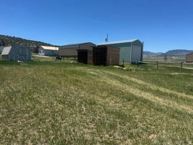 Expansive property featuring multiple outbuildings, including a large green metal structure with an overhead door, a smaller grey shed, and two additional wooden structures