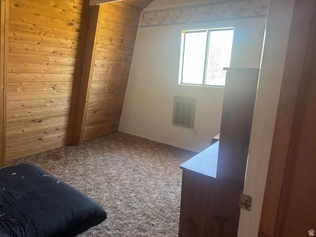 Room featuring wood-paneled accent walls, an angled ceiling, and a built-in wall vent