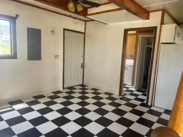 Black and white checkerboard flooring throughout, featuring a paneled interior door with dark trim, a window with dark trim, an exposed electrical panel, and a built-in ceiling fan with light fixture