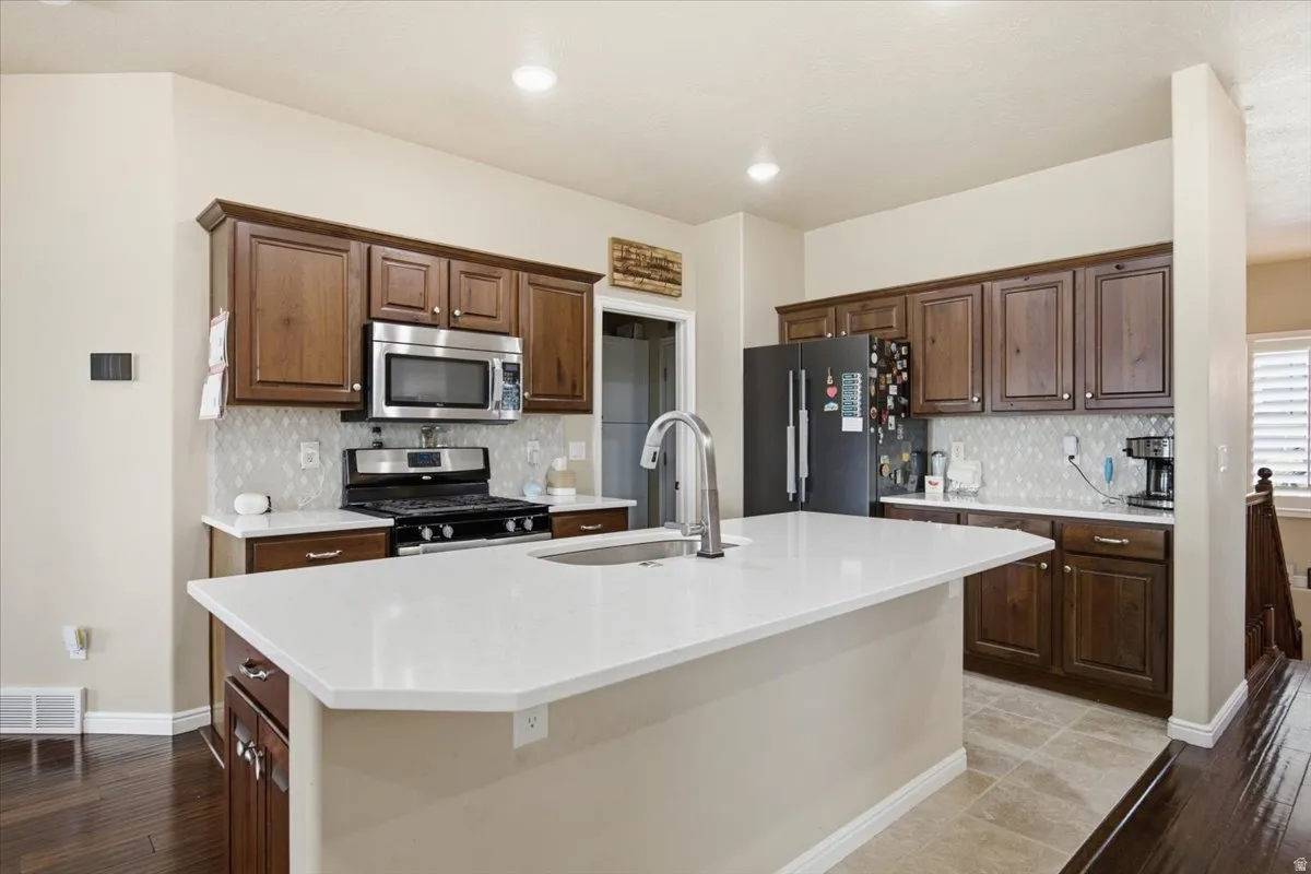 Kitchen featuring a large island with an undermount sink, wood cabinetry, stainless steel appliances, a gas range, and patterned tile backsplash