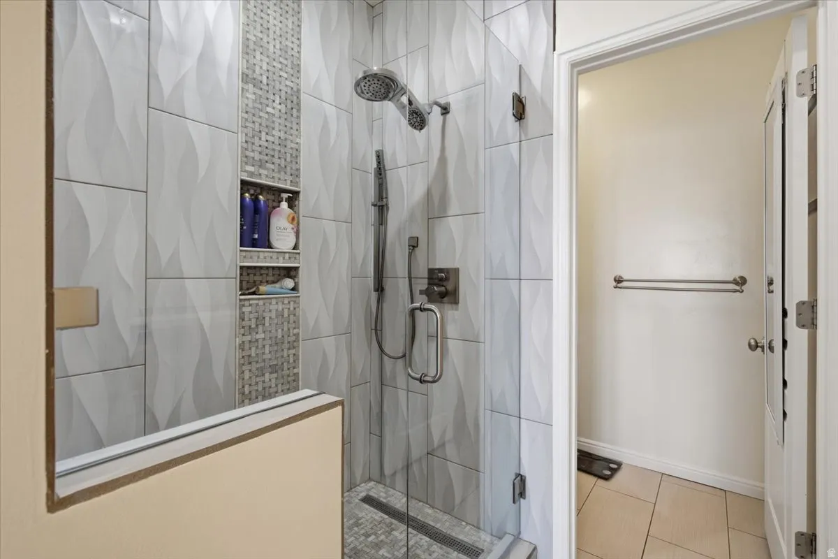 Glass-enclosed shower featuring textured large-format wall tiles, a recessed niche with mosaic accent tiling, a dual shower head system, and a linear floor drain