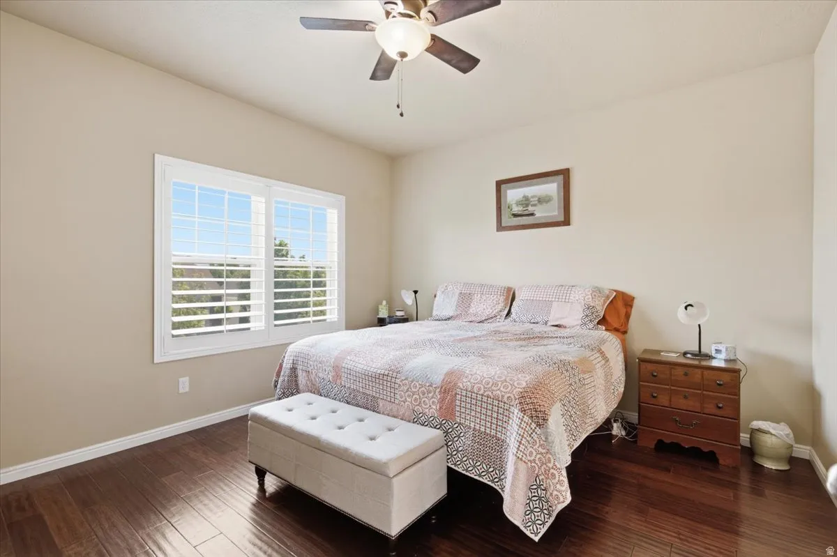 Bedroom featuring wood-finish flooring, a ceiling fan with integrated lighting, and window with plantation shutters