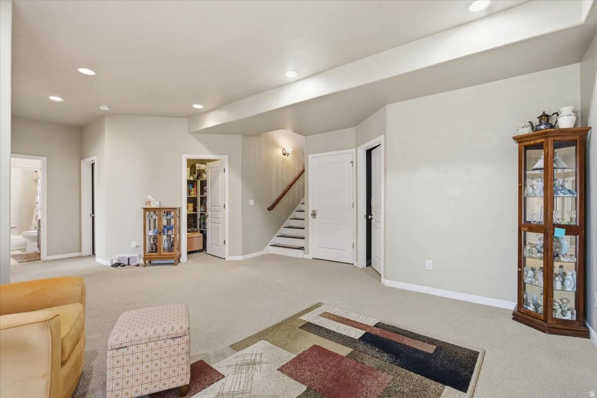 Spacious carpeted room featuring recessed lighting and a visible staircase with wood railing