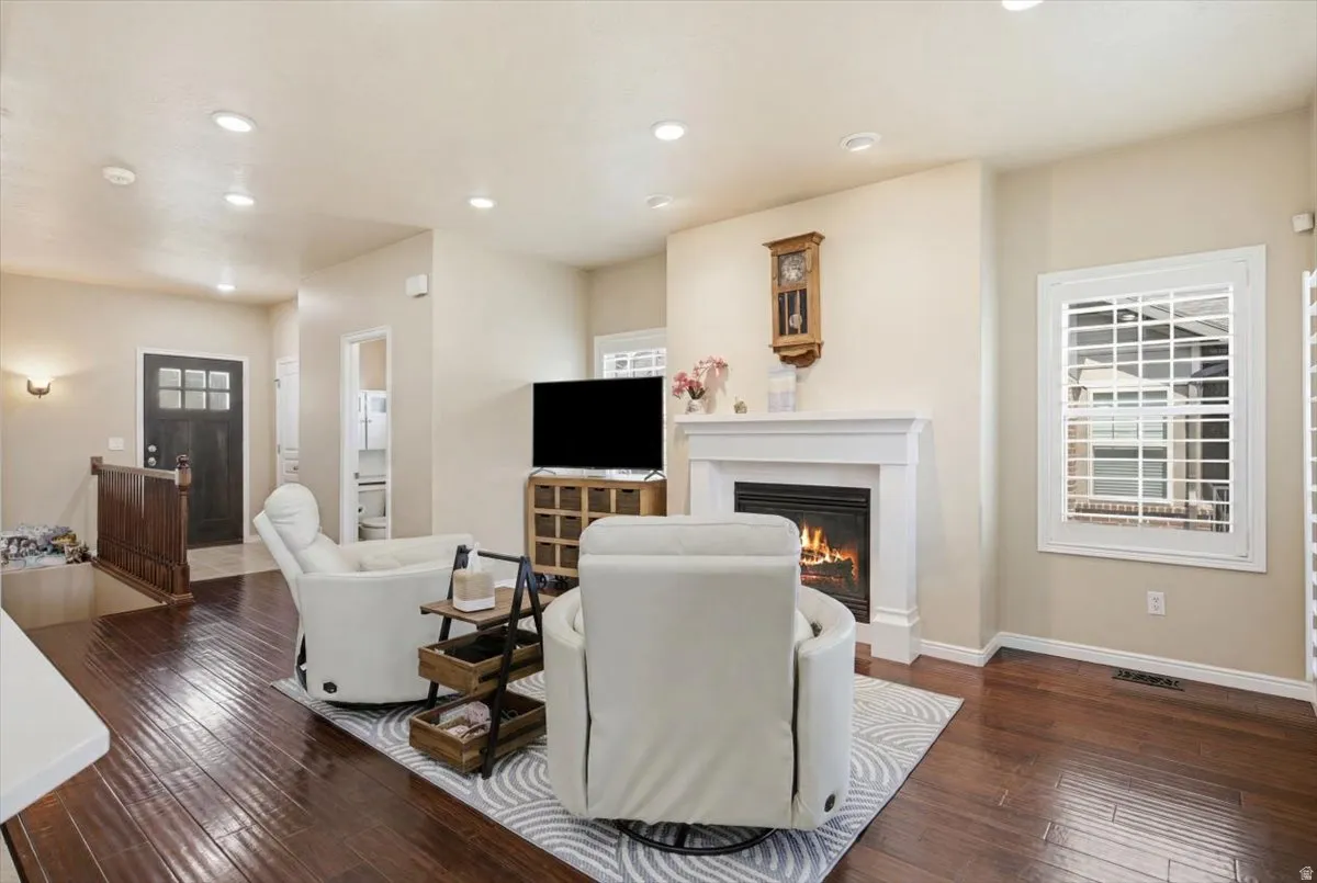 Living area featuring wood-finish flooring, a white mantel fireplace, recessed lighting, and a white plantation-shutter window