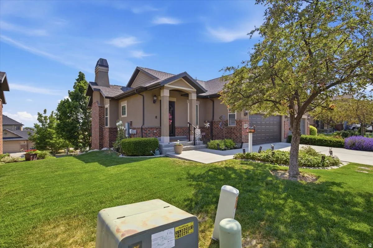 Exterior featuring stucco siding, brick accents, a covered entry, an attached garage, and a lush front lawn with established landscaping