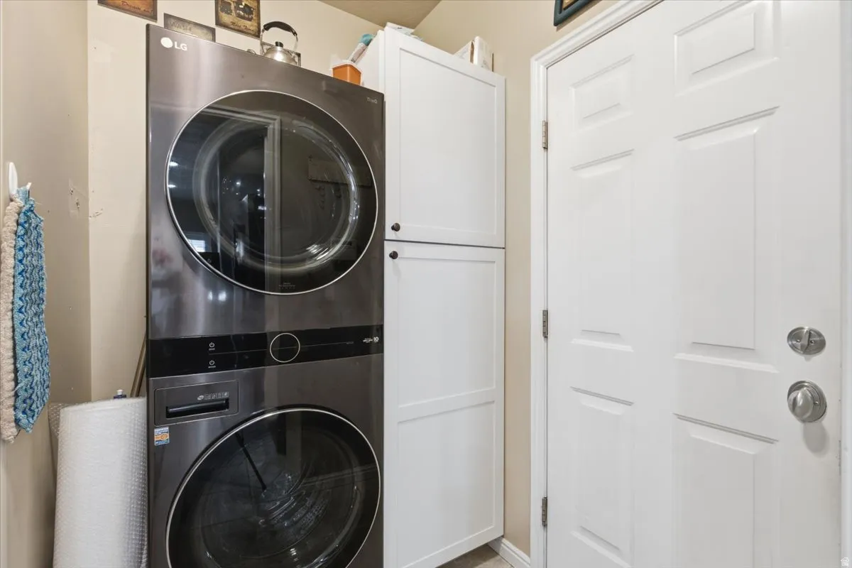 Laundry area featuring a stacked washer and dryer, white paneled cabinetry, and a white paneled door with brushed nickel hardware
