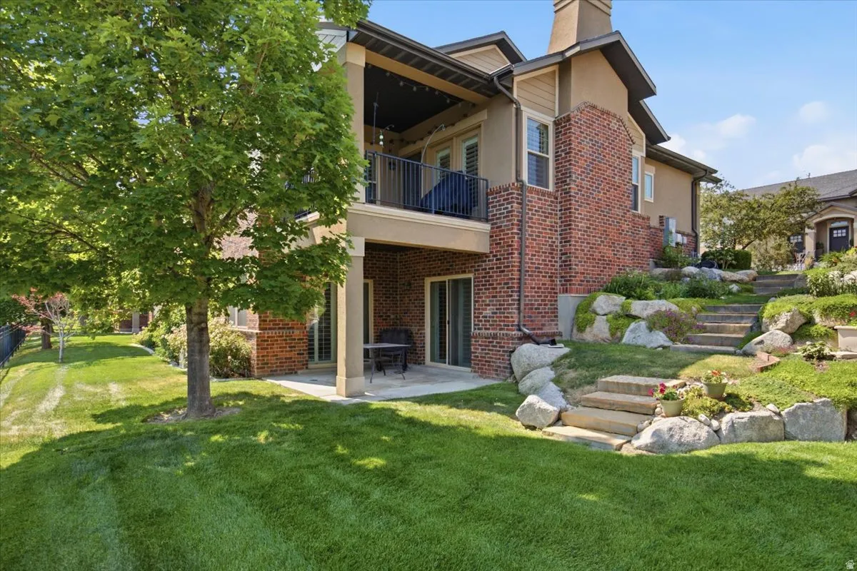 Rear elevation featuring a covered upper-level balcony with metal railings, a lower-level patio, and a tiered stone staircase
