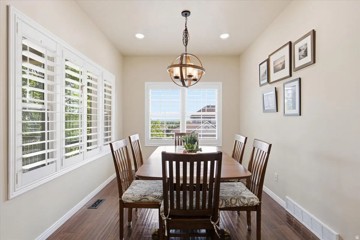 Dining area with wood-finish flooring, white plantation shutters, recessed lighting, and a spherical chandelier