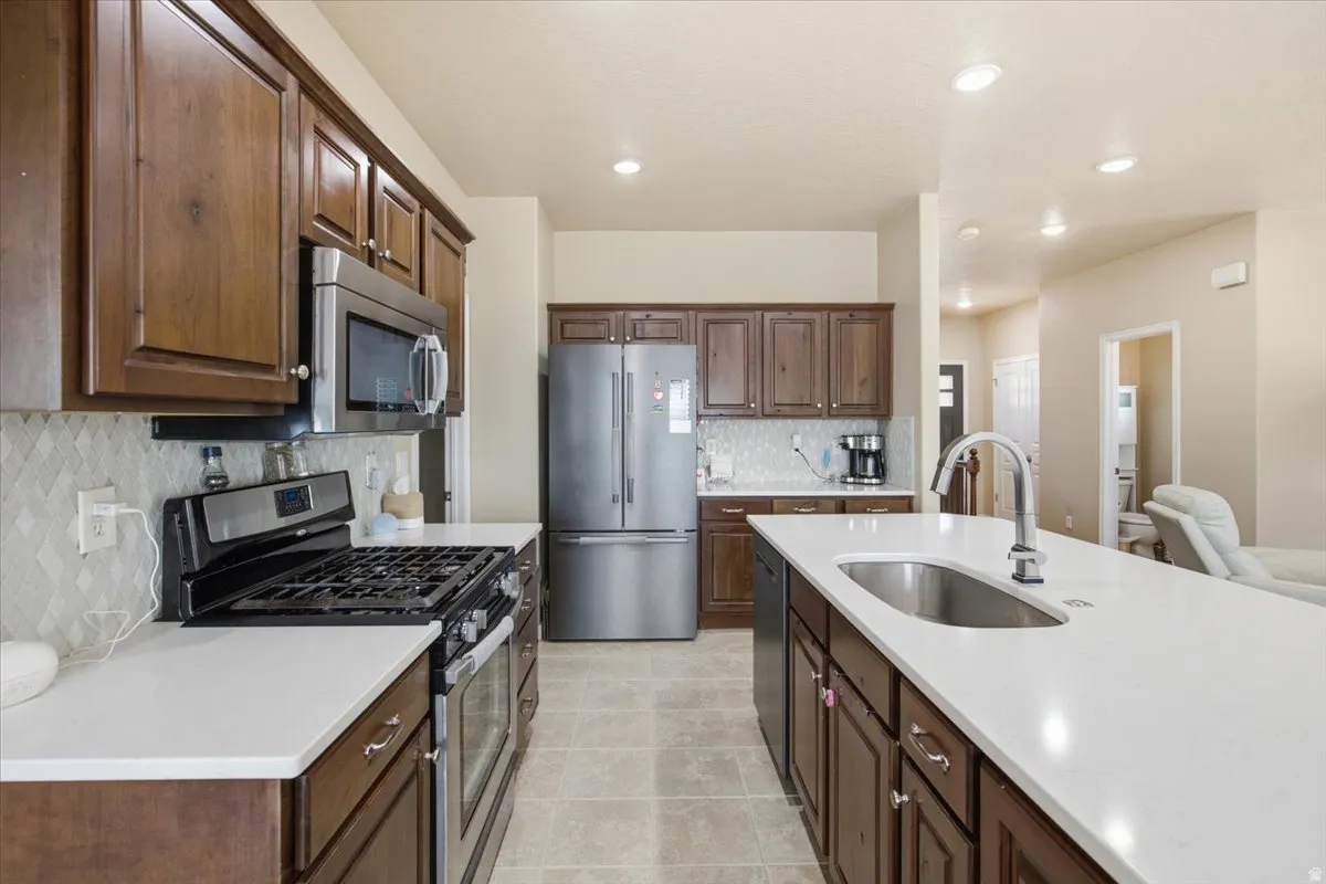 Kitchen featuring stainless steel appliances, dark wood cabinetry, white countertops, and a full tile backsplash