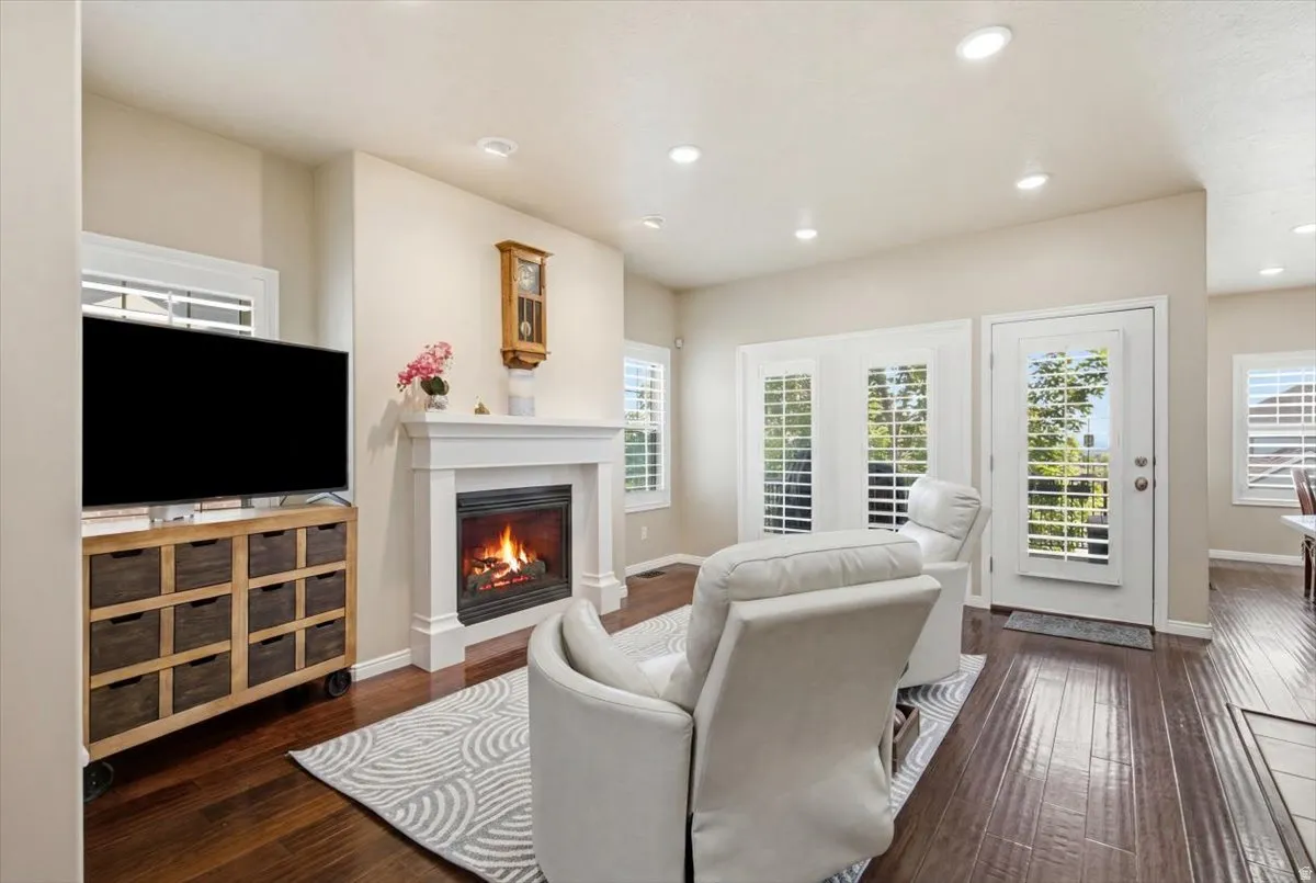 Living area featuring a fireplace with a white mantel, recessed lighting, wood-finish flooring, white plantation shutters, and a glass-paneled door