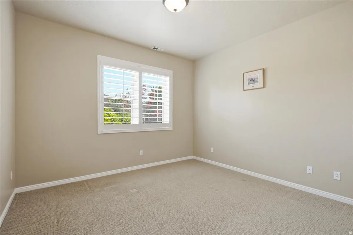 Neutral-toned room featuring a window with white plantation shutters, light beige carpet, and white baseboards