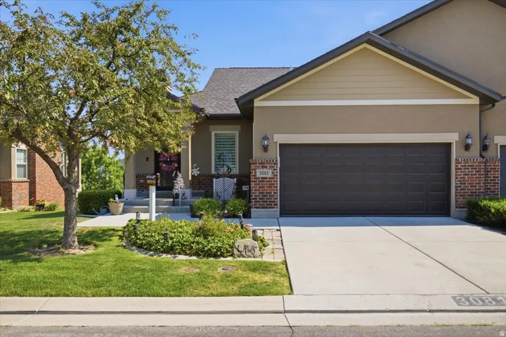 Exterior featuring a two-car garage, brick accents, stucco siding, and a covered porch
