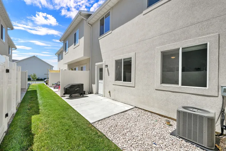 Rear exterior featuring stucco siding, multiple windows, a private concrete patio, and a gravel area