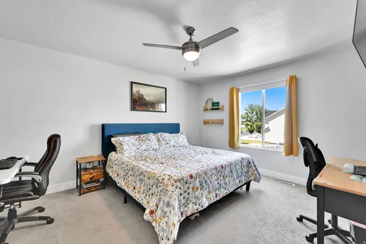 Bedroom featuring light gray carpeting, a large window with yellow drapes, and a ceiling fan with integrated lighting