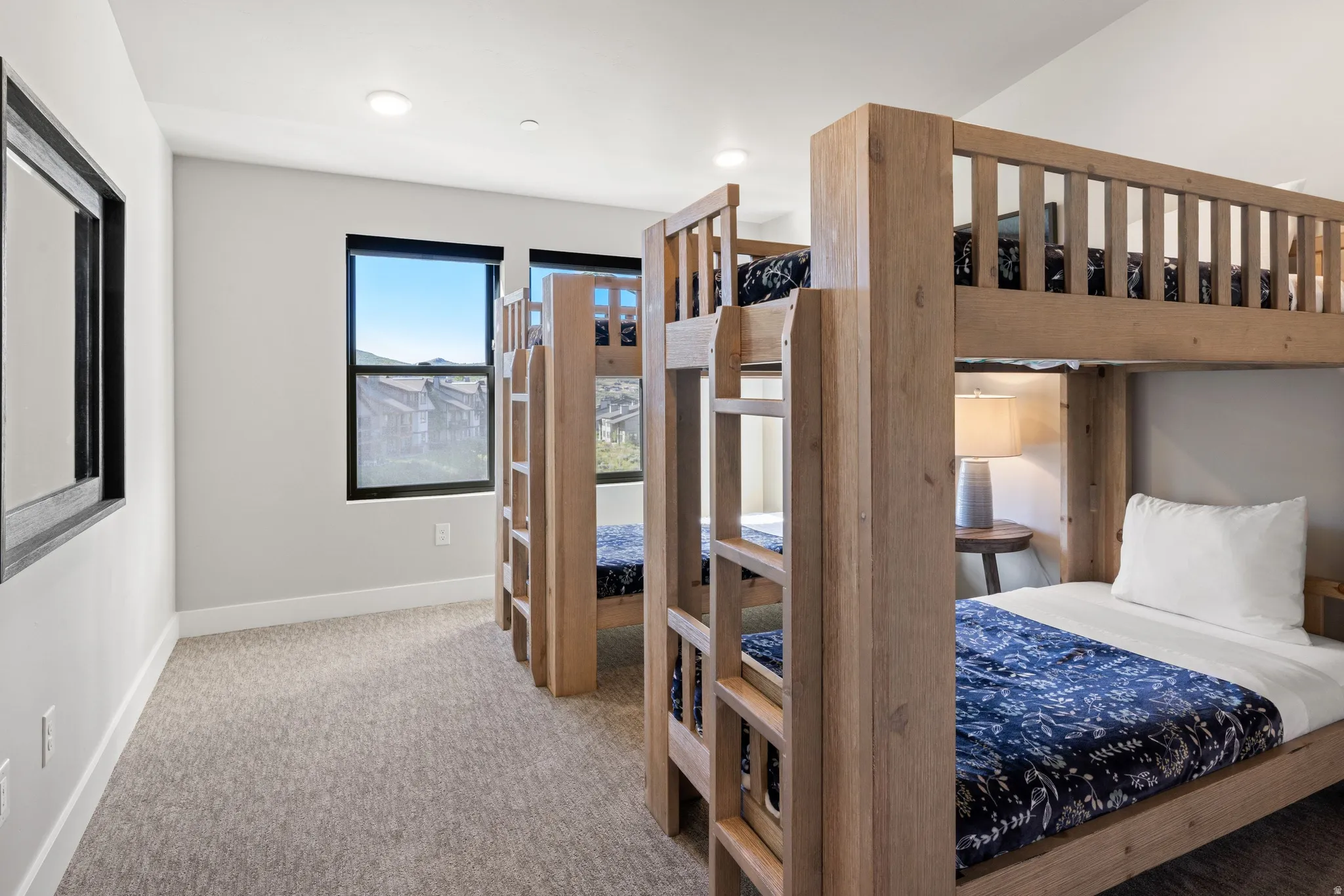Room featuring two bunk bed structures with natural wood finish, light gray carpet flooring, and white painted walls