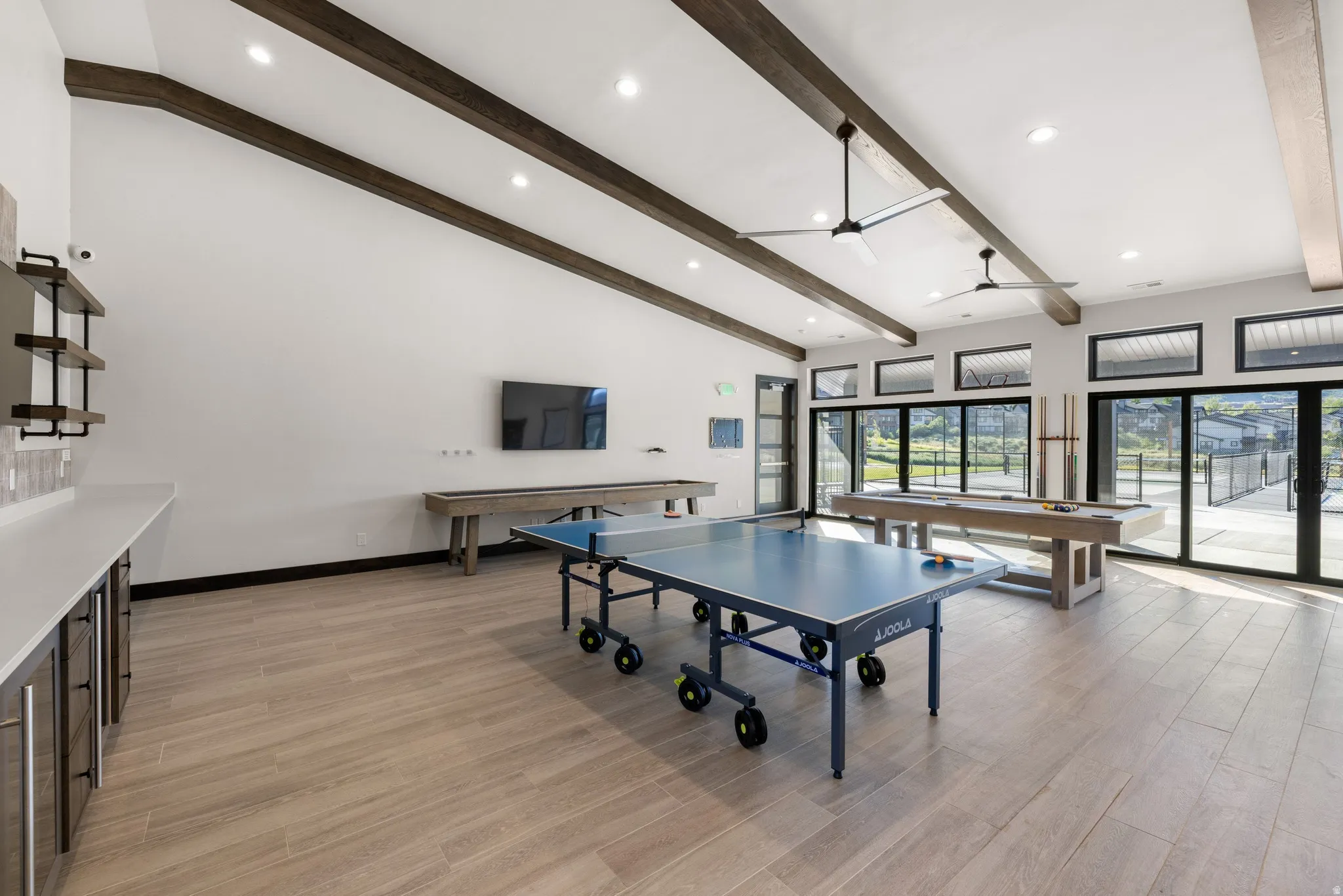Spacious entertainment room featuring wood-finish flooring, vaulted ceilings with exposed beams, and contemporary ceiling fans