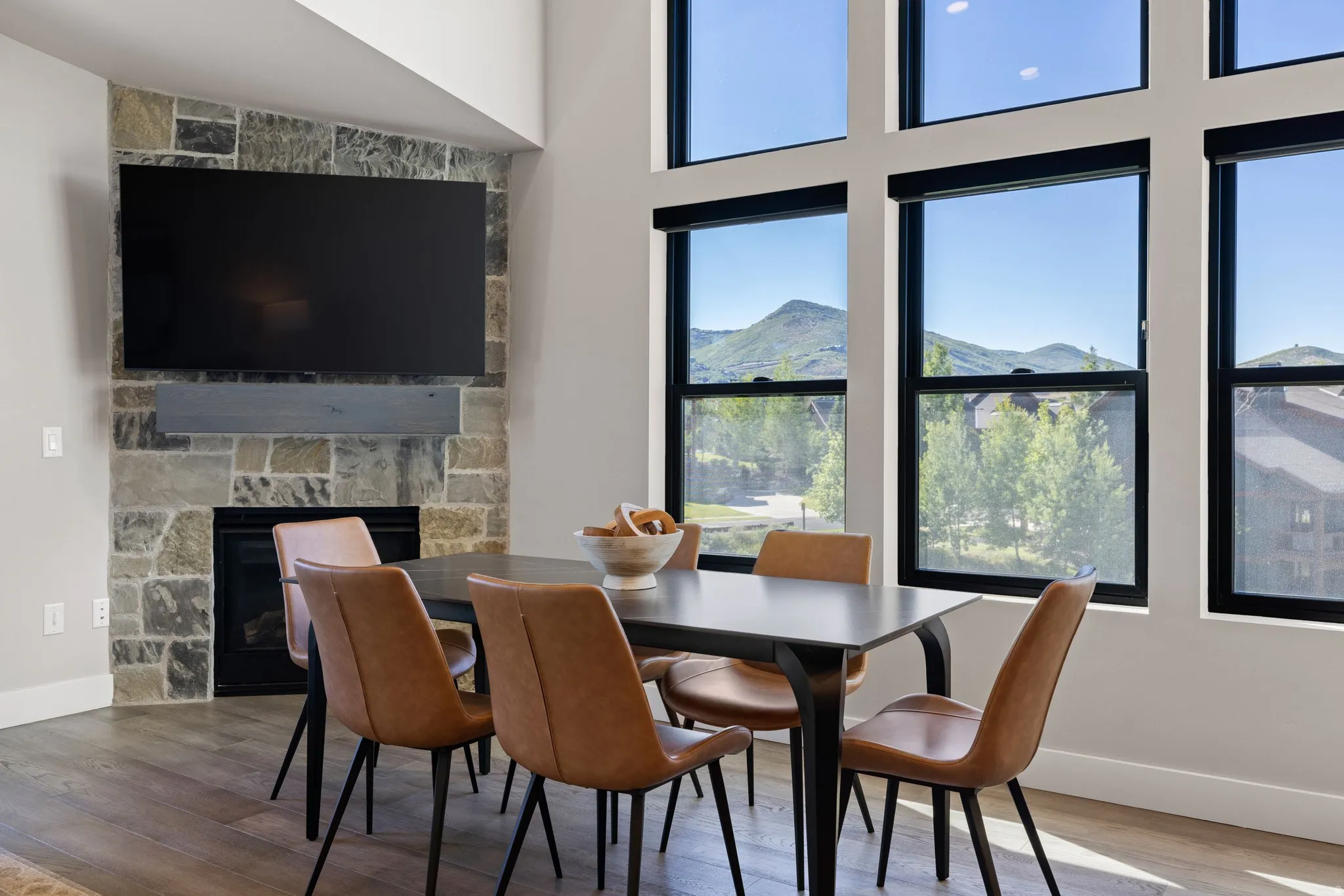Spacious room featuring a stone-faced fireplace with a wood mantle, a mounted flat-screen television, and expansive windows