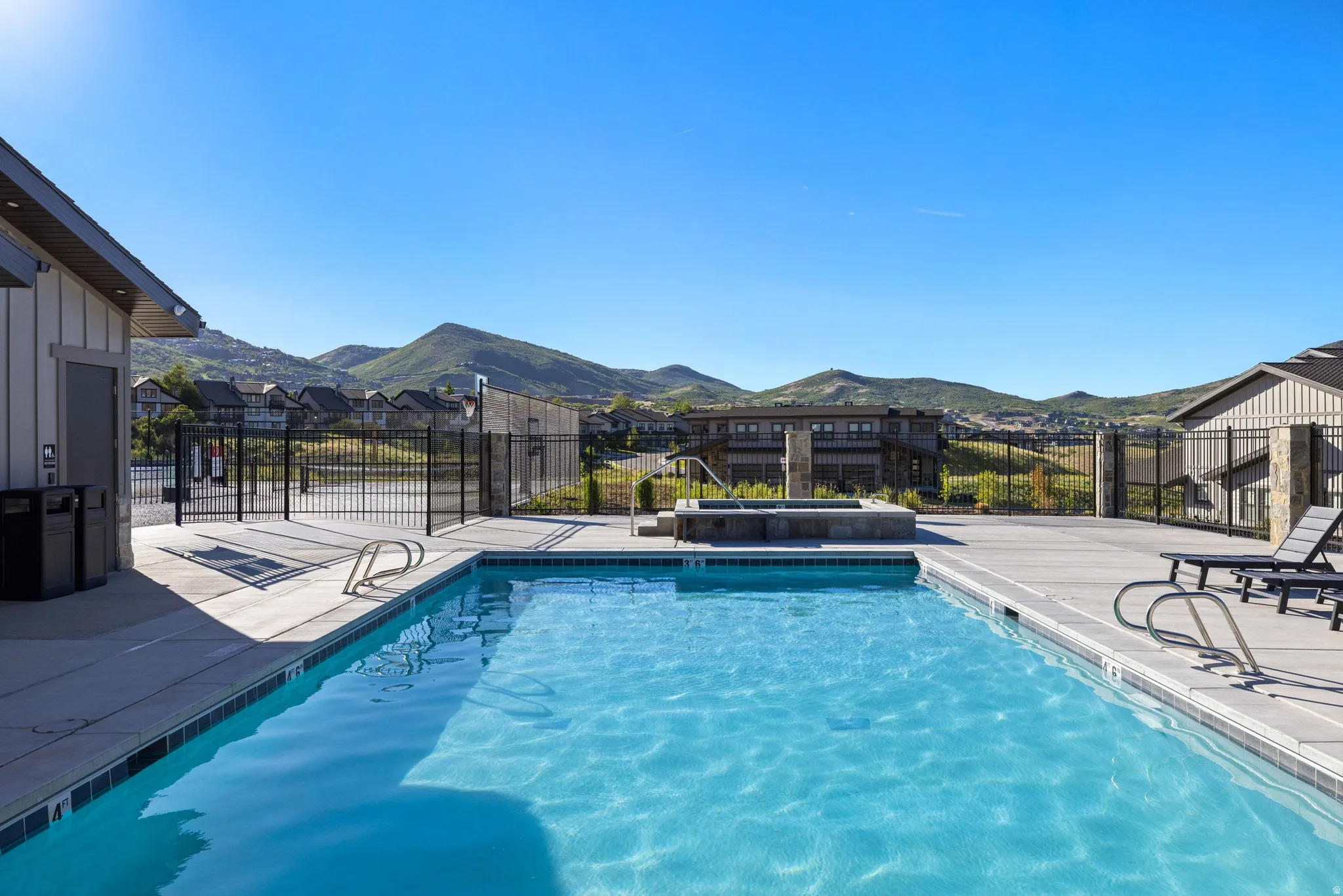 Outdoor swimming pool with concrete decking, a built-in hot tub, and surrounding black metal fencing