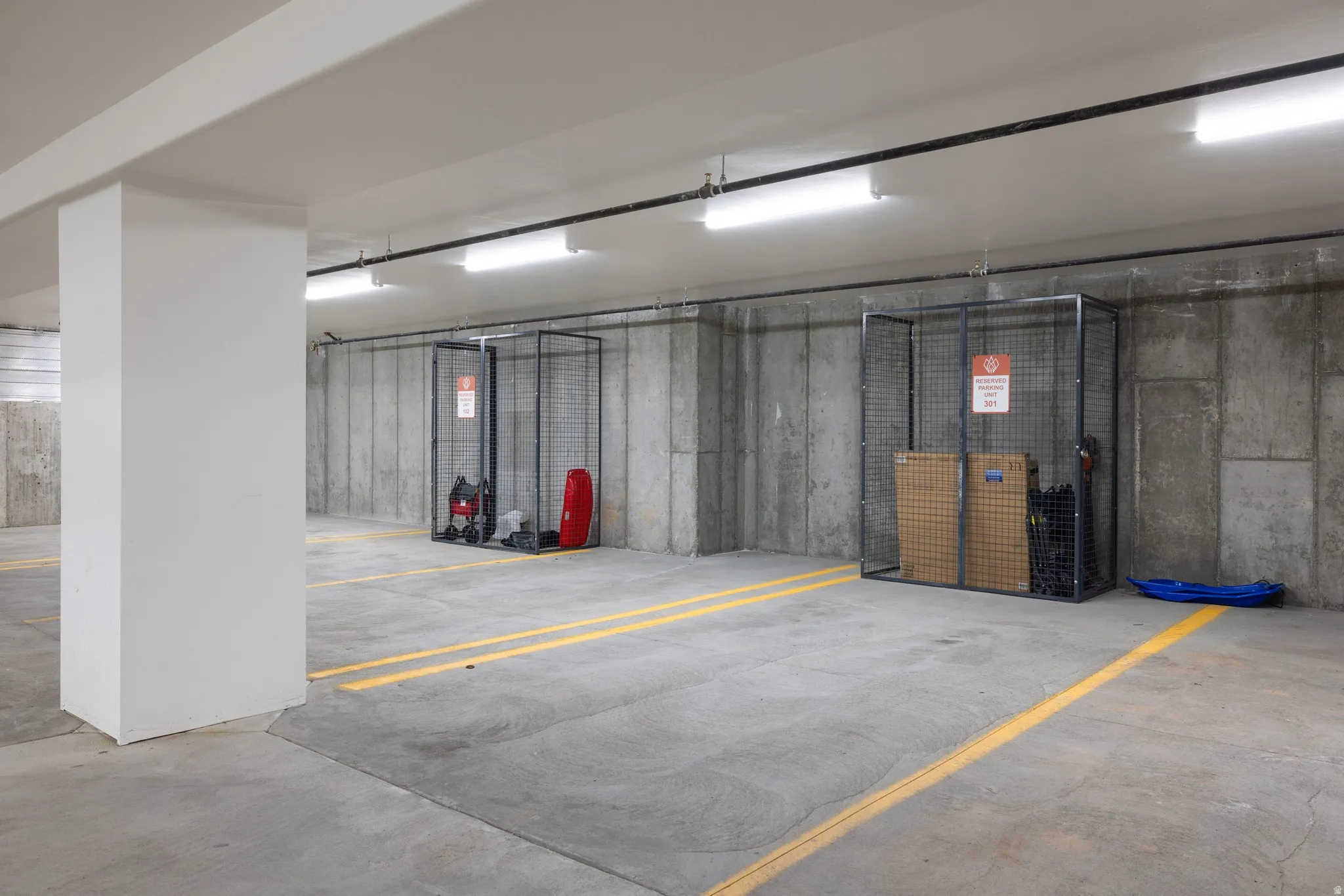 Underground parking garage featuring concrete flooring, overhead fluorescent lighting, concrete walls, and individual metal storage lockers