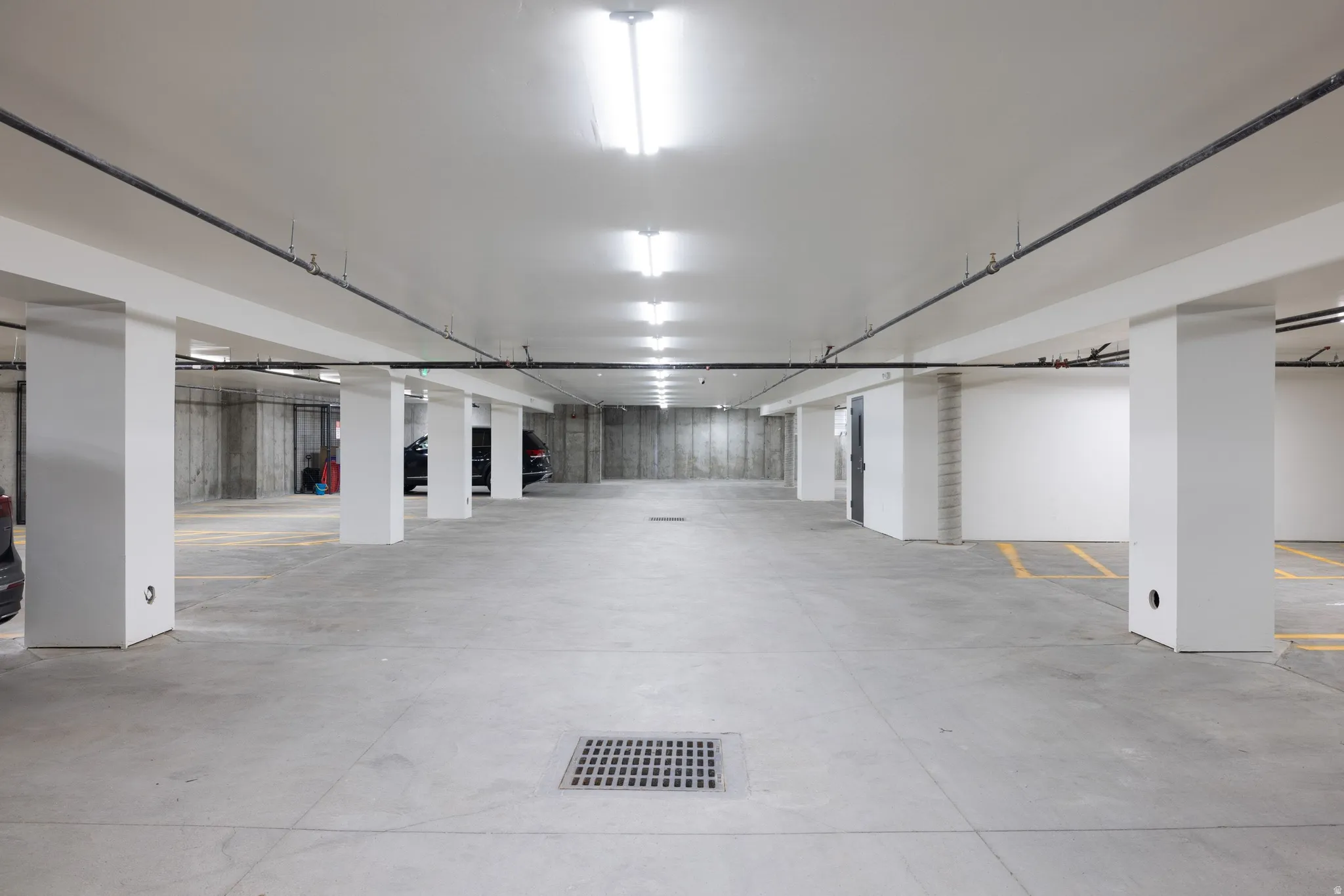 Spacious underground parking garage featuring concrete flooring, exposed concrete walls, white structural columns, and overhead fluorescent lighting