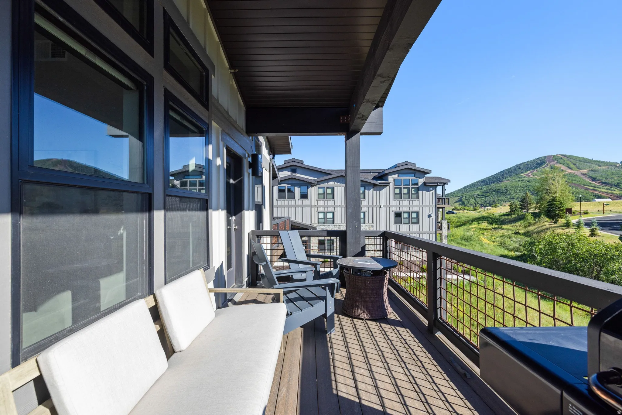 Spacious outdoor balcony featuring composite decking, dark wood railing with mesh infill, and direct mountain scenery