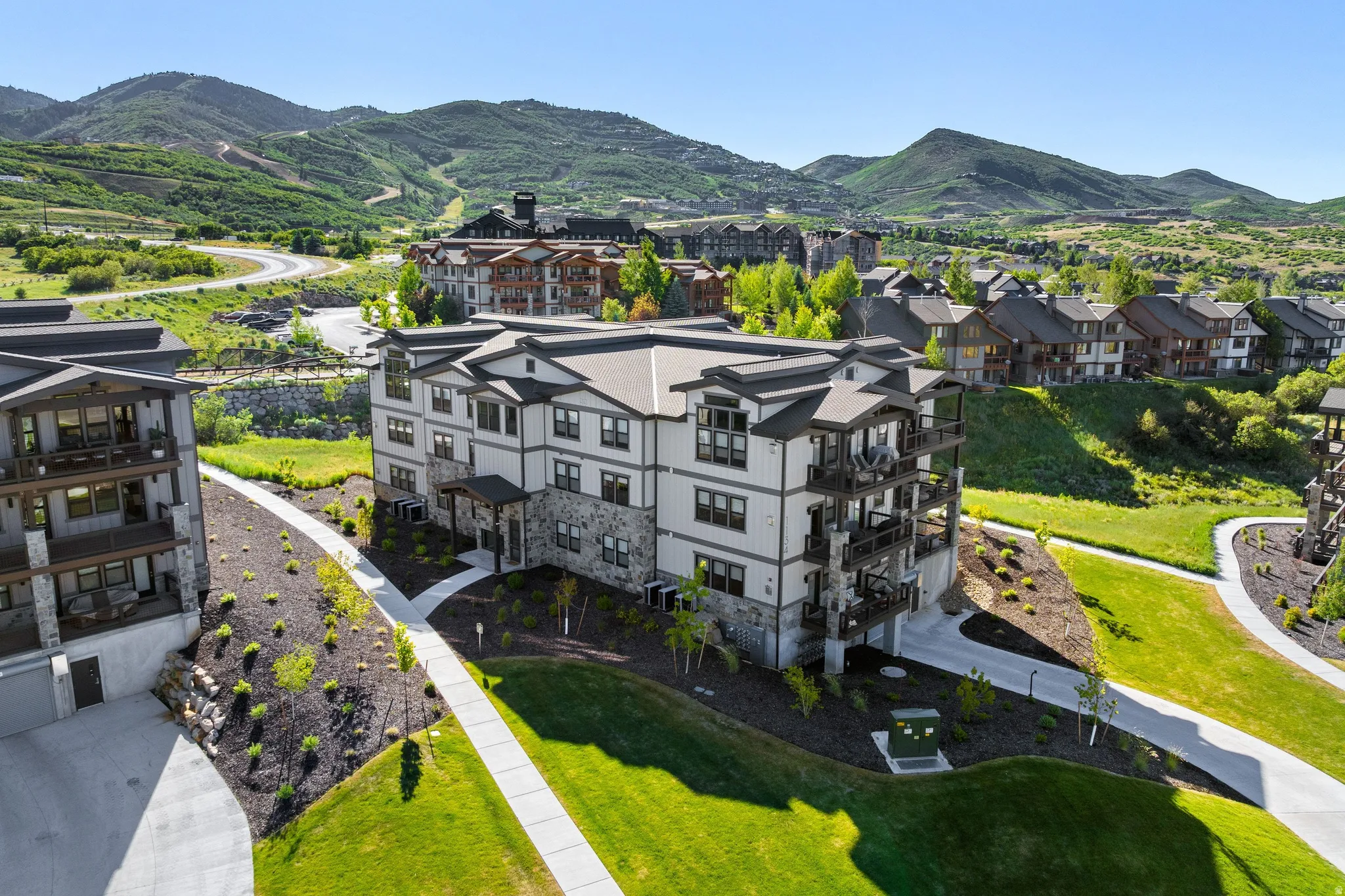Multi-story building featuring stone and siding exterior, private balconies, and a paved walkway surrounded by manicured landscaping