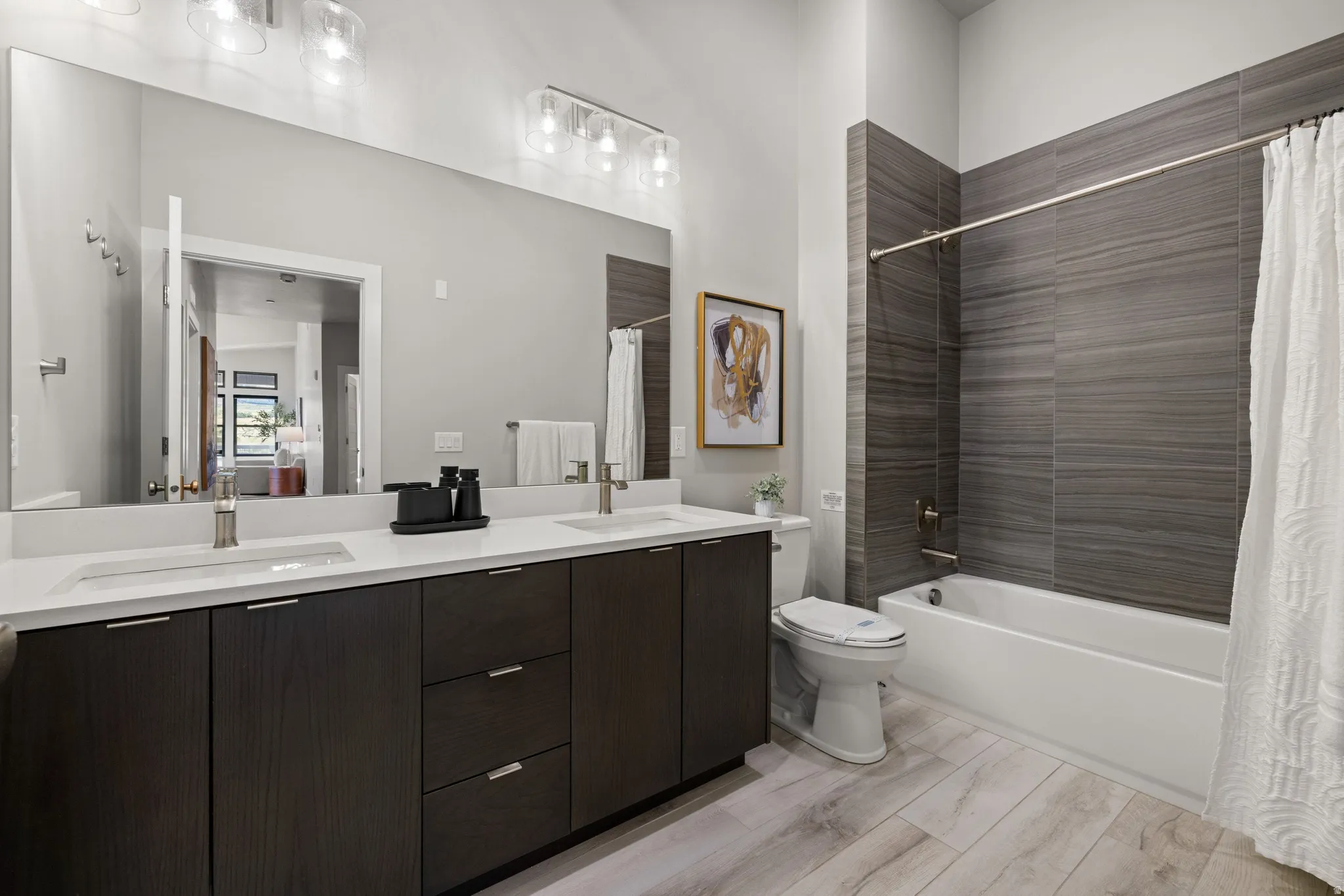 Bathroom featuring a dual vanity with undermount sinks and individual faucets, a full-width mirror, and a combination shower-tub with dark grey wall tiling