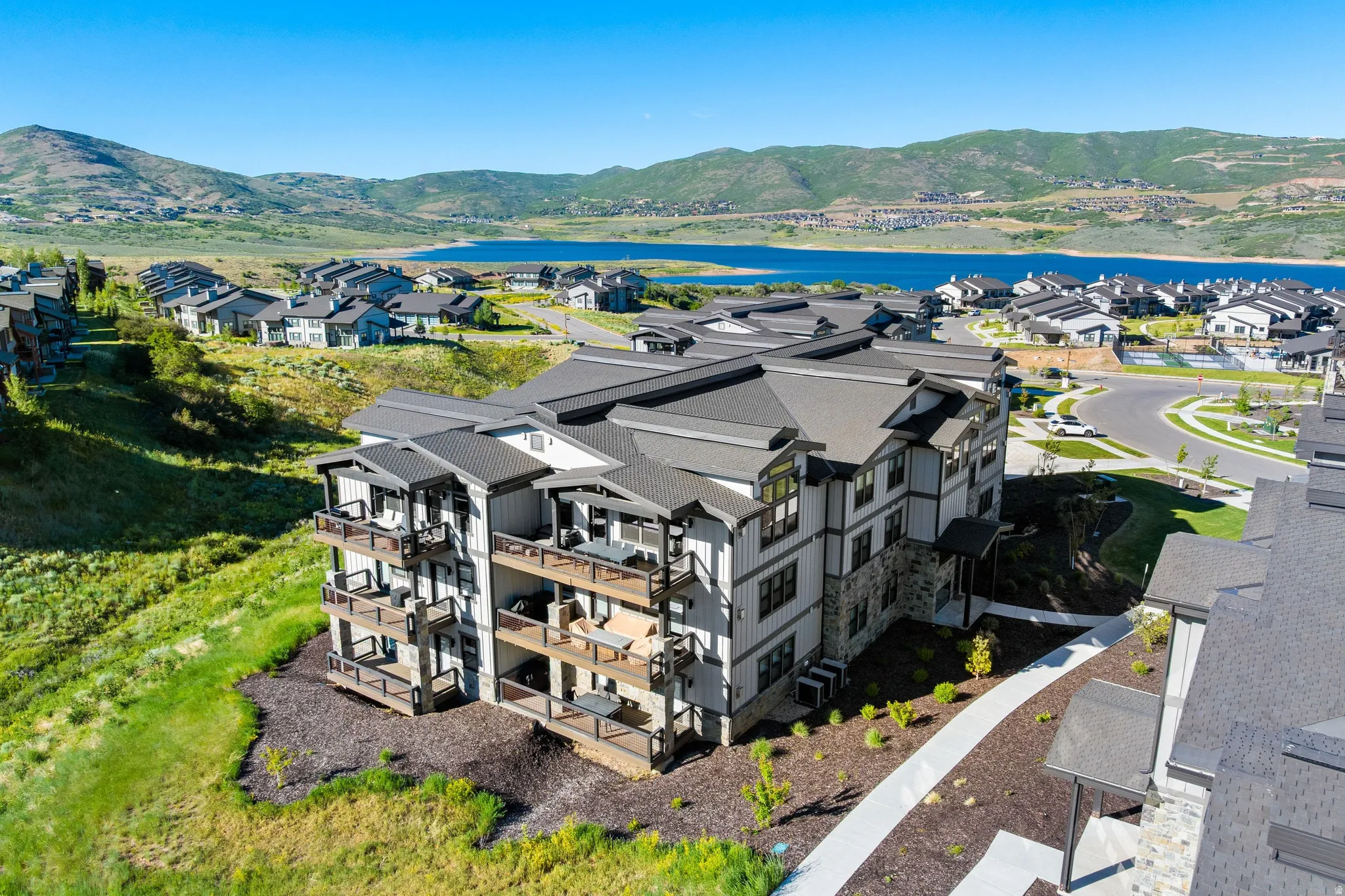 Modern multi-story building featuring stacked balconies, stone veneer accents, vertical siding, and a dark shingle roof