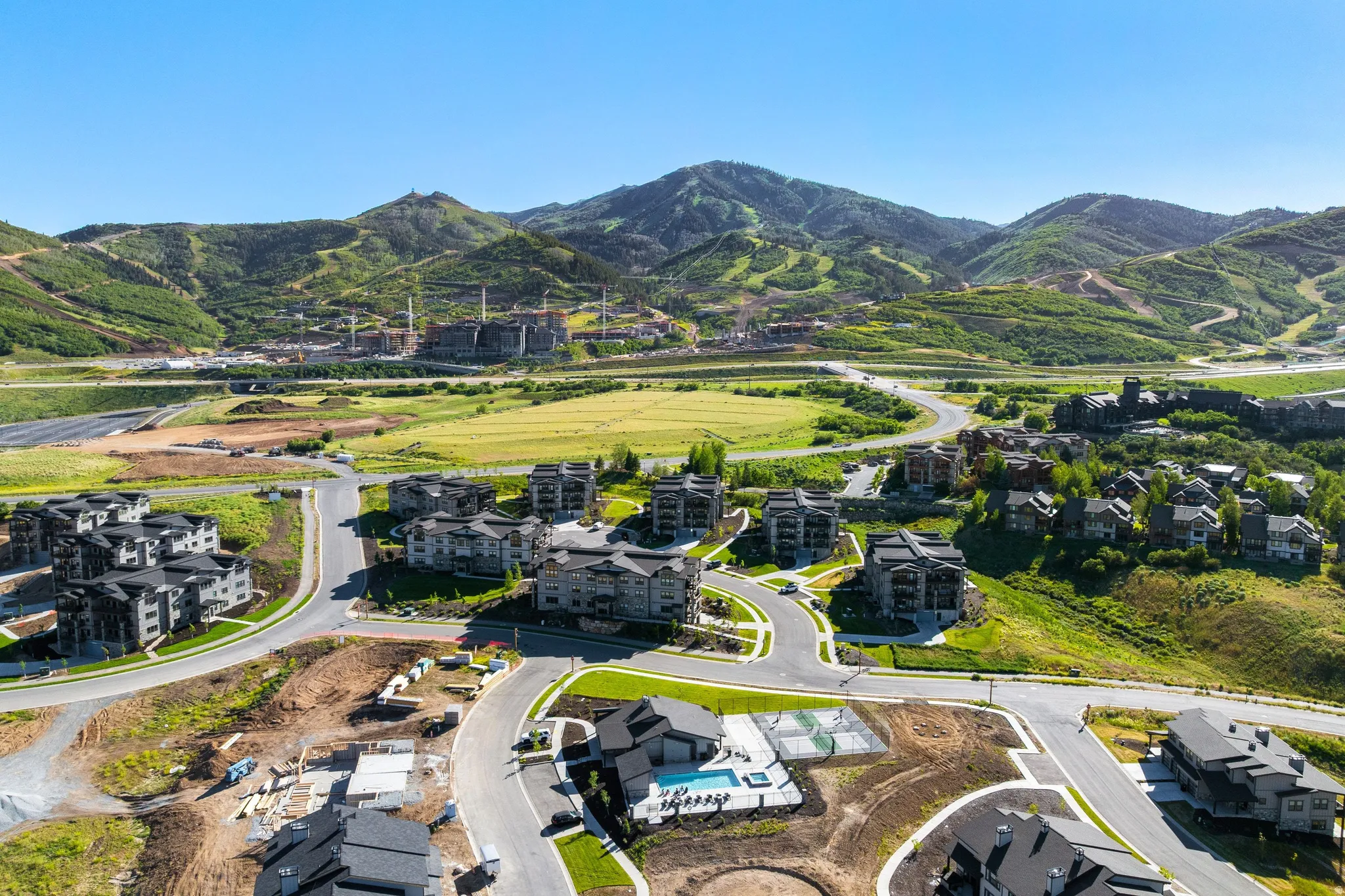 Expansive mountain landscape featuring a developing community with residential buildings, paved roads, and green spaces